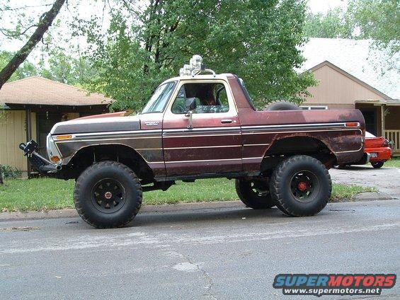 Lifted Ford Bronco with off-road tires and light bar on roof, parked on street