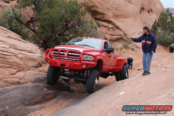 Red Dodge Ram pickup truck with custom bumper navigating rocky terrain, person pointing