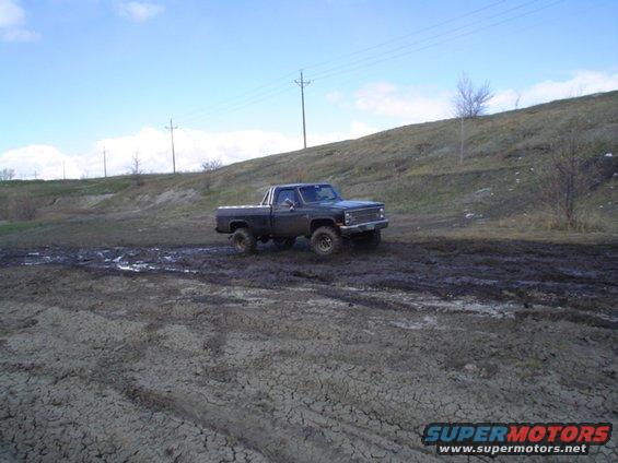 Dark pickup truck with a roll bar driving on a muddy track