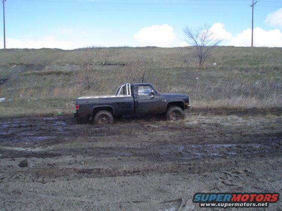 Dark pickup truck with roll bar stuck in mud, side view