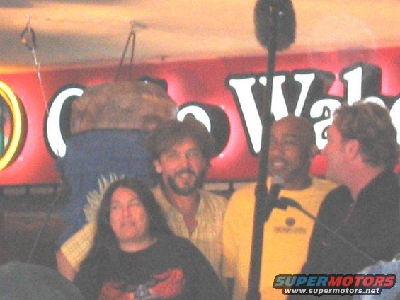 Four people stand in front of a red sign with white lettering that says "Cabo Wabo"