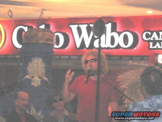 Sammy Hagar sings into a microphone with a Cabo Wabo sign behind him