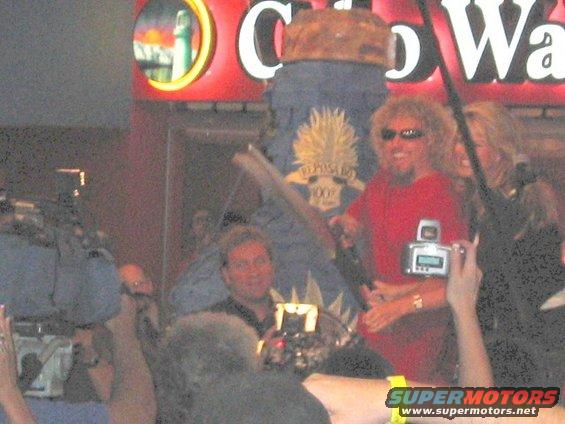 Crowd gathered around a man in a red shirt, with cameras and a sign that says "Cabo Wabo"