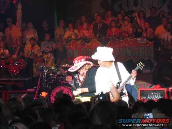 Musicians playing on a stage in front of a crowd, with a banner behind them