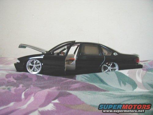 Black toy car with hood and doors open, sitting on a patterned surface
