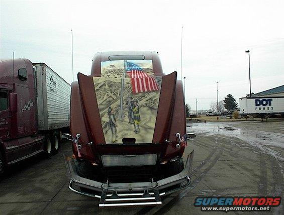 Semi-truck hood painted with 9/11 theme, showing firefighters and American flag. Another semi-truck is parked to the left