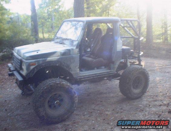 Suzuki Samurai with roll cage and off-road tires parked on dirt road