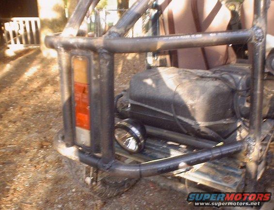 Rear of a heavily modified off-road vehicle with a custom roll cage, external fuel tank, and aftermarket lights