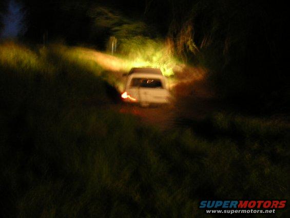 White SUV driving on a dirt road at night, headlights on