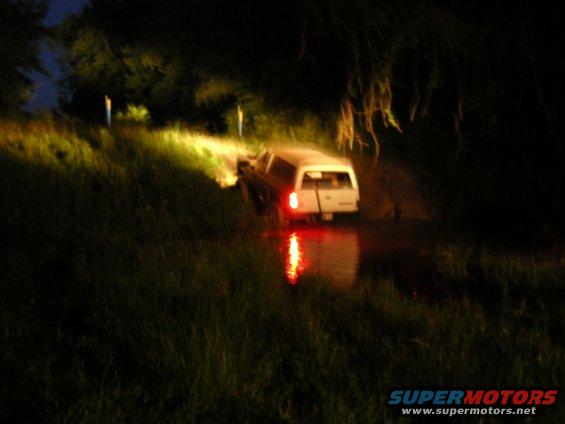 White pickup truck with camper shell driving through water at night, headlights on
