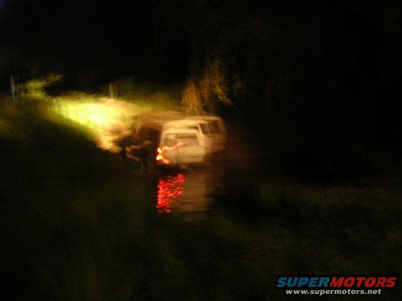 White van with its brake lights on, parked on the side of a dark, grassy road