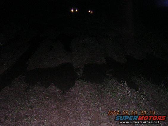 Two bright headlights shine in the dark night over a grassy area