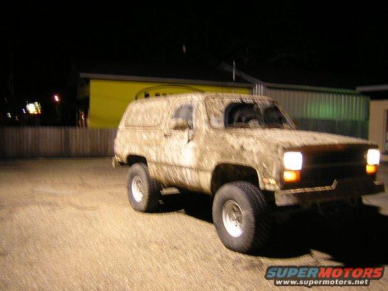 Mud-covered SUV parked at night. The vehicle has large tires and appears to be a Chevrolet K5 Blazer from the early 1980s