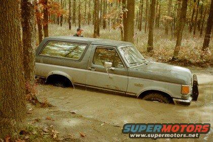 Ford Bronco stuck in a muddy forest clearing, front bumper visible