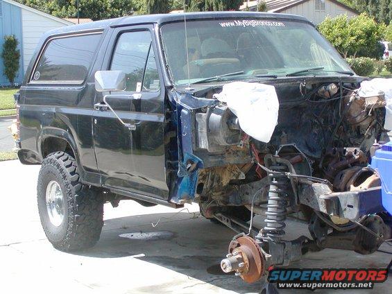 Black Ford Bronco with front end disassembled, showing engine components and suspension. A website URL is visible on the windshield