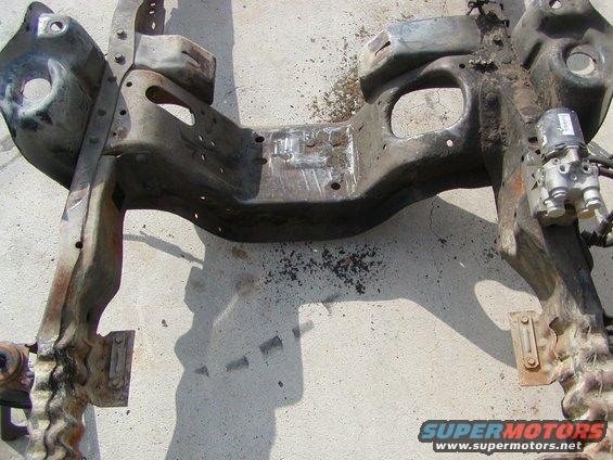 Rusty metal vehicle frame section with hydraulic components attached, lying on concrete