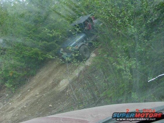 Dark green Jeep Wrangler climbing a steep dirt hill off-road