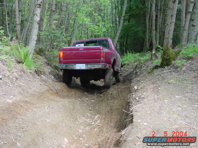 Red 1992 Ford F-150 pickup truck driving on a dirt trail, rear view