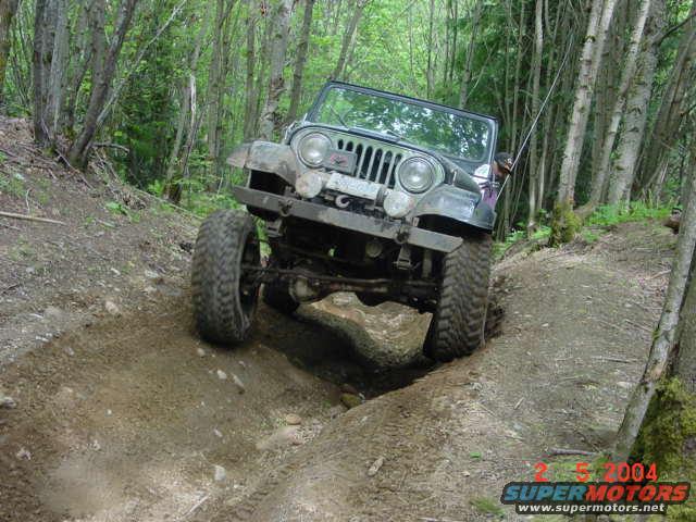 Jeep CJ-7 climbing a dirt trail in a forest