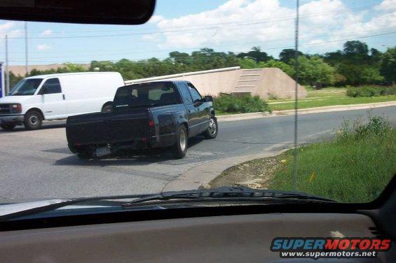 Black pickup truck driving on a road, white van in background