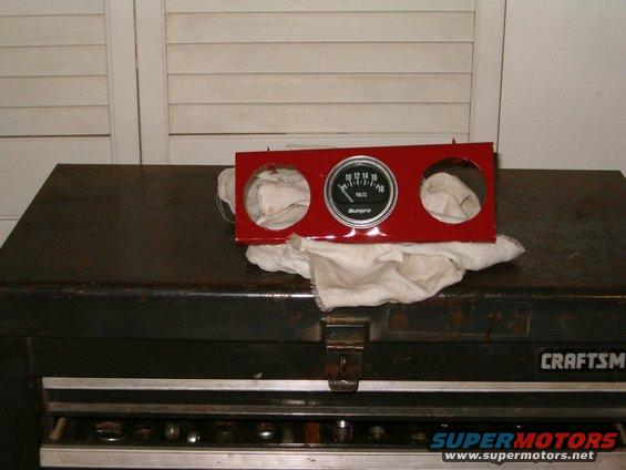 Red gauge cluster with a Sunpro voltmeter, resting on a white cloth atop a black toolbox