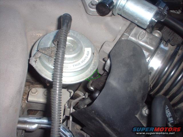 Close-up of engine components including a round metal part with a hose and a black plastic intake manifold
