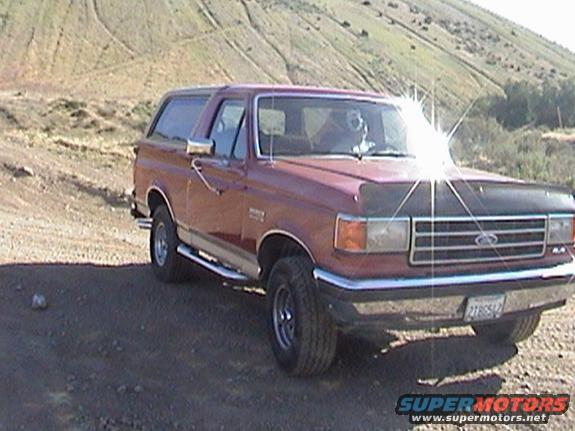 Red 1990 Ford Bronco parked on dirt road with hills in background