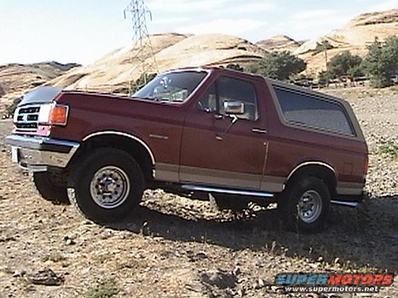 Maroon Ford Bronco SUV with tan trim, parked on dirt terrain