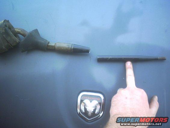 Dodge emblem on a dark surface with a car part held by a finger