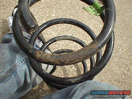 Two black coil springs, one nested inside the other, with visible rust and a green tag on the upper spring