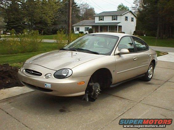 Gold 1999 Ford Taurus sedan with front passenger wheel removed, parked on a concrete driveway