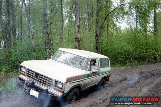 White 1978 Ford Bronco stuck in mud on a dirt road, front winch visible