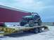 1992 Ford Bronco - A custom-built green off-road buggy is transported on a flatbed trailer, with a large red barn in the background.