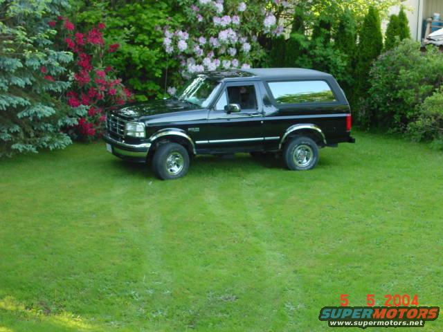 Black 1992 Ford Bronco parked on a green lawn with bushes and flowers in the background