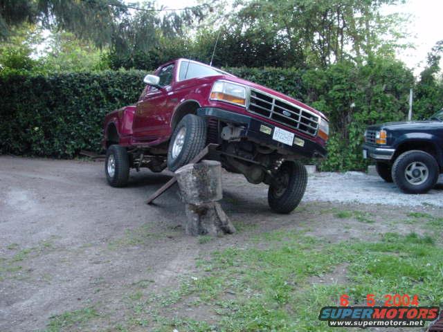 1992 Ford F-150 front end angled up on a log, with another truck beside it
