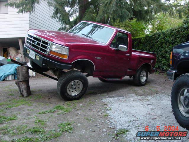 Red 1992 Ford F-150 pickup truck on blocks, front end raised