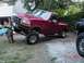 1992 Ford F-150 - A red 1992 Ford F-150 pickup truck is propped up on blocks, with another dark-colored vehicle visible to the right.