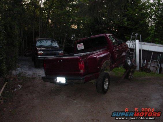 Red pickup truck with a "For Sale" sign in the window, lifted on a stand, rear view