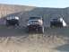 2000 Ford F-450 - Three trucks are parked on sand dunes under a clear sky. The middle truck is a dark color with off-road lights.