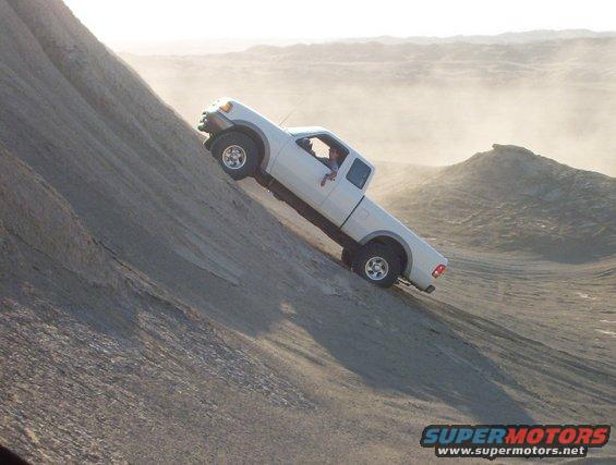 White pickup truck driving up a steep dirt hill. Driver is visible
