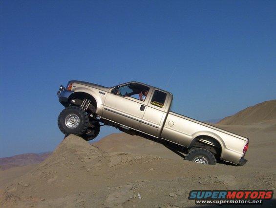 Gold 2000 Ford F-450 pickup truck with lifted suspension driving on a sand dune