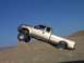 2000 Ford F-450 - A gold 2000 Ford F-450 pickup truck navigates a steep sand dune under a clear blue sky.