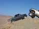 2000 Ford F-450 - Two pickup trucks navigate challenging terrain on a sunny day, with one truck climbing a steep sand dune.