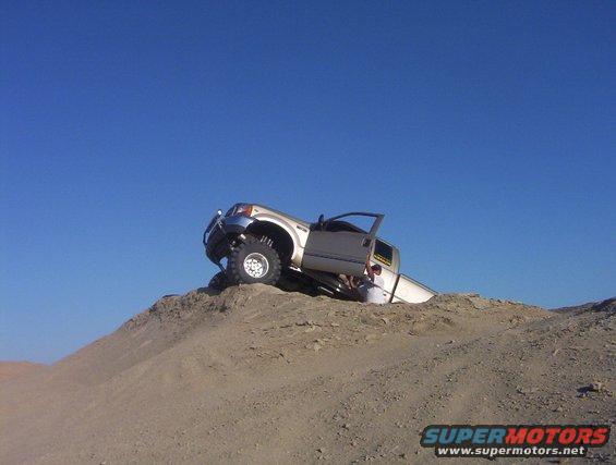 Silver 2000 Ford F-450 on its side on a sand dune, driver's door open