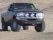 2000 Ford F-450 - A black pickup truck with off-road tires and auxiliary lights is parked on a dirt surface.