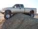 2000 Ford F-450 - A lifted silver Ford F-450 pickup truck is positioned on a dirt incline under a clear sky.