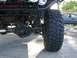 1996 Ford Bronco - Close-up of an off-road vehicle's front suspension and tire, with a sedan visible in the background.