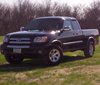 Black Toyota Tundra pickup truck, front 3/4 view, parked on grass with trees in background