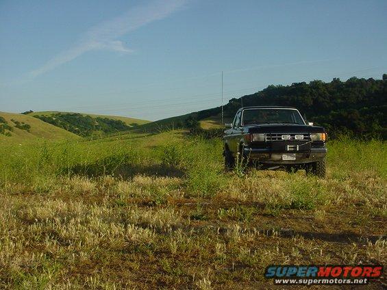 Black Ford F-Series truck parked in a field with rolling hills behind it