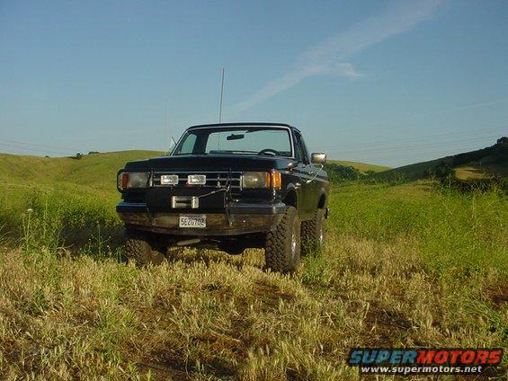 Black pickup truck with winch parked in a grassy field under a blue sky